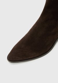 Bottine en cuir suédé marron avec un bout pointu et une texture lisse, présentant une semelle fine et un design épuré.
