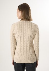 Beiger, kabelgestrickter Pullover mit strukturiertem Muster, langen Ärmeln und geripptem Saum, von hinten vor einem neutralen Hintergrund präsentiert.