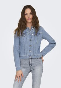 Chaqueta de mezclilla azul claro con cierre de botones, dos bolsillos en el pecho y un diseño ligeramente ajustado. Tejido texturizado con detalles de costura visibles.