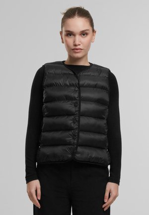 Bélelt fekete mellény elöl patentgombokkal, steppelt dizájnnal és kerek nyakkivágással. Hosszú ujjú fekete felső fölött viselve.