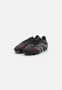 Crampons de football noirs avec une surface texturée, accentués par des lignes rouges et grises, présentant un design traditionnel à lacets et six crampons sur la semelle.
