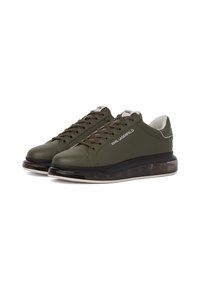 Sneakers verde oliva con una toma in pelle liscia, punta tonda e suola traslucida a pattern. Presentano lacci e un logo bianco sul lato.