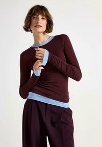 Top met lange mouwen in diep bordeauxrood met lichtblauwe accenten bij de halslijn en manchetten, met een aansluitend ontwerp en zachte, rekbare stof.