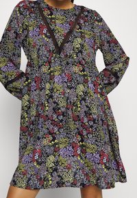 Šaty s květinovým vzorem, které mají námořnický podklad, dlouhé rukávy, výstřih ve tvaru V s dekorativní krajkou a volný střih.