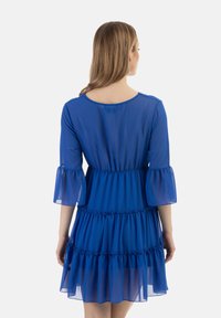 Rochie din chiffon albastru cu mâneci până la trei sferturi, volane suprapuse și un croi lejer. Prezintă un gât rotund și accente volan la mâneci.