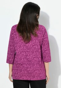Blouse à motif floral violet avec des manchons trois-quarts et une coupe décontractée. Le tissu semble léger, avec une texture lisse.