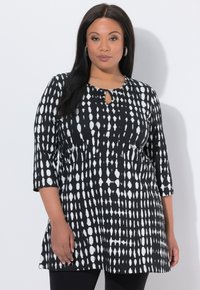 Czarna i biała tunika z dekoltem w kształcie dziurki od klucza, rękawami do połowy przedramienia oraz wzorem wydłużonych kropek i abstrakcyjnych kształtów. Gładka faktura tkaniny.