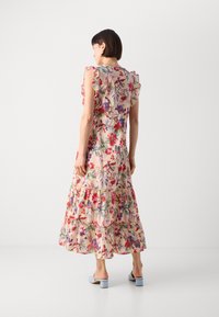 Rochie maxi florală de culoare bej deschis cu volane în straturi. Prezintă flori vibrante roșii și mov, precum și o transparență subtilă. Este asortată cu pantofi cu toc bloc de culoare albastru deschis.