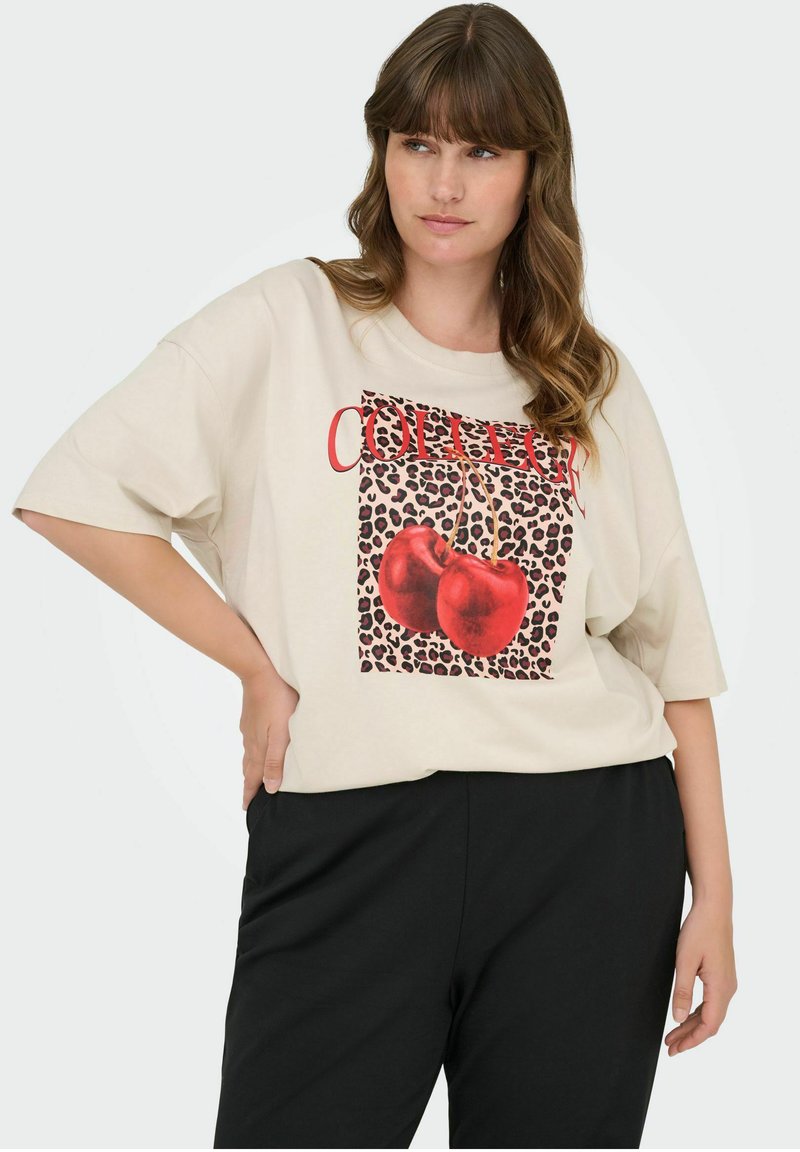 Beżowy, oversize t-shirt z graficznym motywem przedstawiającym czerwone wisienki na tle w leopardzie wzory oraz napis "College" w kolorze czerwonym.