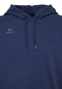 Felpa con cappuccio blu navy dal morbido texture, dotata di tasca a marsupio frontale, lacci con punte in metallo e un piccolo logo sul petto.