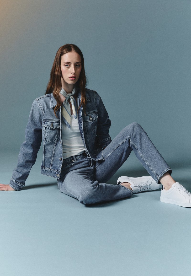 Denim jacket and jeans in light blue, paired with a white top and a patterned scarf. White sneakers complete the outfit. Smooth texture.