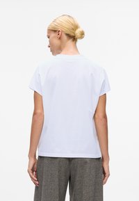 Weißes Baumwoll-T-Shirt mit kurzen Ärmeln, lockerer Passform, rundem Ausschnitt und schlichter Rückseite, kombiniert mit grauen Hosen.