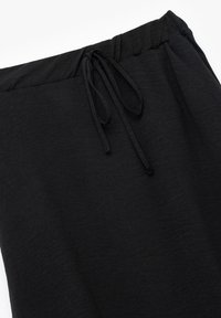 Pantalons noirs à cordon de serrage en tissu texturé, dotés d'une taille élastique et d'un subtil éclat. Design léger et ample.
