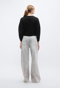 Μαύρο πουλόβερ με στρογγυλ ή λαιμόκοψη και μακριά φουσκωτά μανίκια, συνδυασμένο με τζιν παντελόνι υψηλής μέσης σε ανοιχτό γκρι χρώμα και φαρδιά μπατζάκια, με πίσω τσέπες.