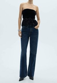 Top negro sin mangas con detalles fruncidos en la cintura, combinado con unos jeans flared de tiro alto en azul y unos tacones negros de punta con tachuelas.