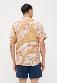 Camisa de tie-dye de manga corta con un patrón en espiral en tonos naranja, rosa y beige, confeccionada en una tela ligera y con un corte relajado.