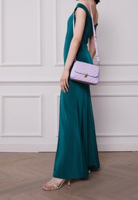 Abito fitted in teal con design off-shoulder; borsa imbottita lavanda con hardware dorato; tacchi a strappo verdi pallidi; sfondo in legno.