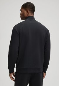 Zwarte trui met een hoge kraag, lange mouwen en geribde manchetten. Glad weefsel, zonder zichtbare patronen of accenten.