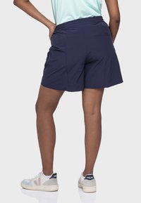 Marineblaue Shorts mit einer lockeren Passform, elastischem Bund und dezenten Stickdetails. Kombiniert mit grau-weißen Turnschuhen.