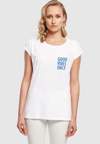 Weißes Baumwoll-T-Shirt mit umgekrempelten Ärmeln, mit blauer Aufschrift "GOOD VIBES ONLY" auf der linken Brustseite. Weicher Stoff, lockere Passform.