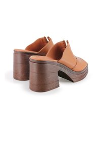 Zuecos de cuero marrón con tacón, punta redondeada, parte trasera abierta y tacón de madera texturizada. Presentan herrajes en tono dorado y un acabado suave.