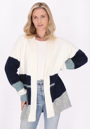 Gebreide cardigan in crème, marineblauw en grijs met brede mouwen, open voorkant en variërende kleurvlakken. Ribbelaccenten bij de manchetten en de zoom.