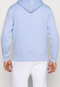 Hoodie blu chiaro con tasca kangaroo frontale, polsini e orlo a coste. Tessuto morbido, vestibilità comoda e coulisse regolabile sul cappuccio.