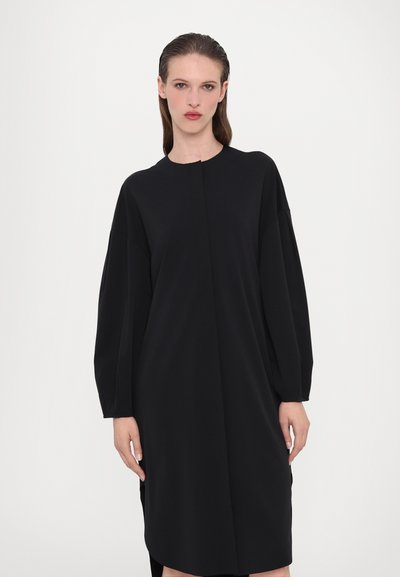 Vestido preto de mangas longas com um decote redondo, feito de um tecido macio. Apresenta um corte reto e fendas laterais para maior liberdade de movimento.