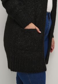 Czarny sweter cardigan z dzianiny, wykonany z teksturowanej tkaniny, z prążkowanymi mankietami i przednią kieszenią. Dokładne odwzorowanie kolorów oraz szczegóły projektu zawarte.