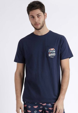 Camiseta de algodón azul marina con mangas cortas, cuello redondo y un bolsillo en el pecho que presenta un diseño gráfico con la frase "Sigue las Olas".