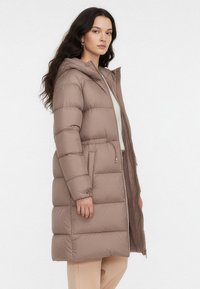 Kurtka puchowa w jasnobrązowym kolorze, z kapturem, zamkiem błyskawicznym i pionowym pikowaniem. Posiada boczne kieszenie i jest o długości do połowy uda.