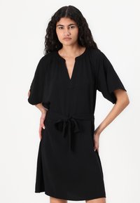 Μαύρο φόρεμα με V ντεκολτέ, κοντά μανίκια και ζώνη στη μέση με κόμπο. Φτιαγμένο από ελαφρύ ύφασμα με άνετη εφαρμογή και πλαϊνές σχισμές.