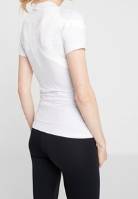 Bílé sportovní tričko s žebrovanou texturou, krátkými rukávy a grafickým detailem na zadní straně s nápisem "ACTIVE SPINE."