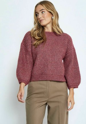 Pletený svetr v barvě burgundy s texturovaným vzorem, kulatým výstřihem a oversized balónovými rukávy, doplněný béžovými kalhotami.