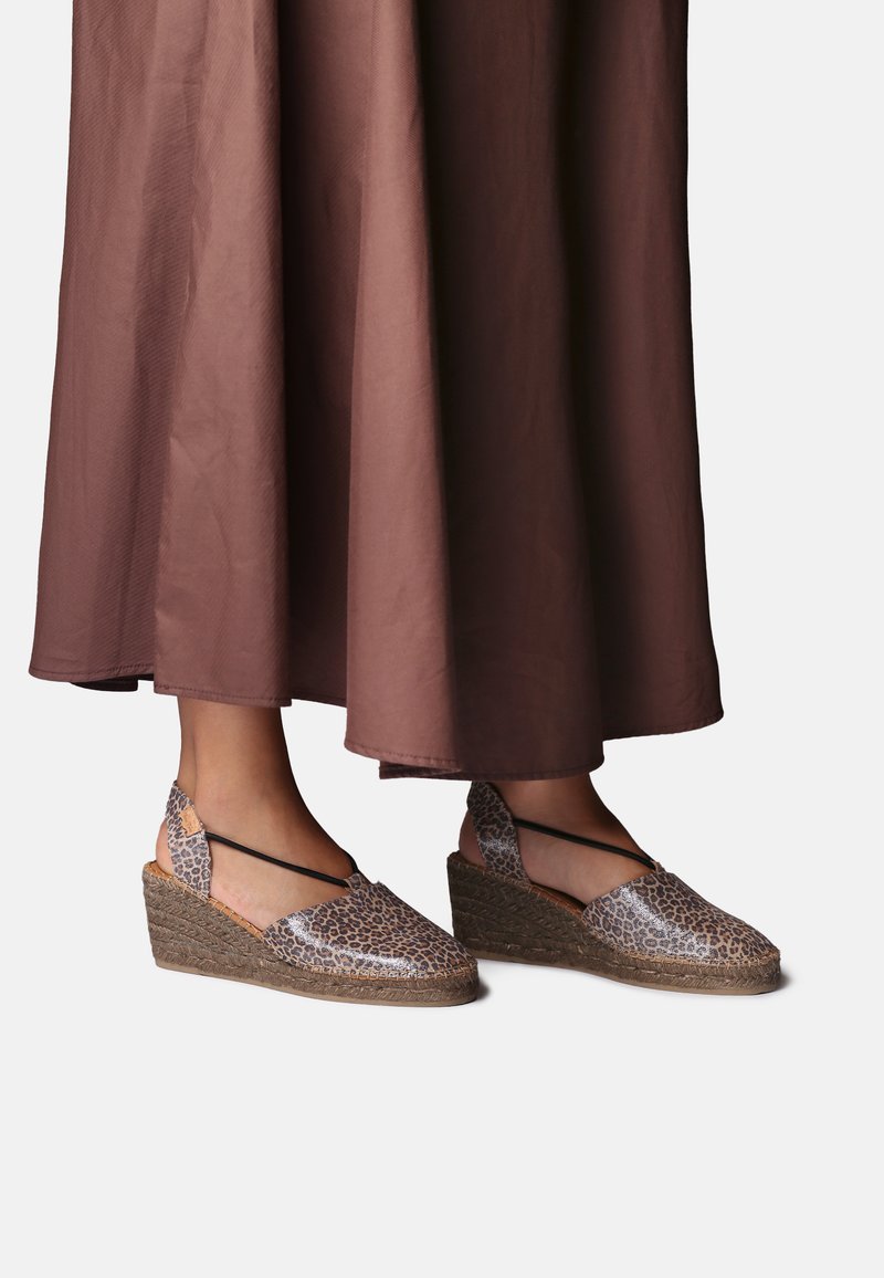 Voeten met bruine wedge espadrilles met luipaardprint en enkelbandjes, gecombineerd met een lange bruine rok.