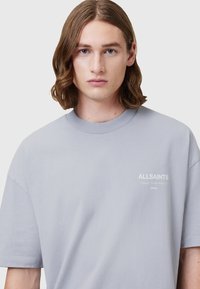 Tricou scurt cu mânecă scurtă, de culoare gri deschis, confecționat din bumbac, cu guler rotund și cu logo-ul "ALLSAINTS" imprimat pe piept.