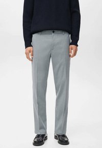 Pantalones grises a rayas con una tela ligera, que presentan un corte ajustado, frente plano y un cierre con un solo botón. Combinados con un suéter oscuro.