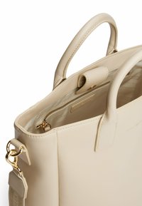 Borsa a tracolla in pelle beige con doppi manici, una tasca principale con zip e dettagli in metallo dorato.