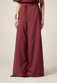 Brede burgundy broek van lichtgewicht stof met een elastische tailleband en koord. Gecombineerd met puntige rode hakken en een multicolor armband.