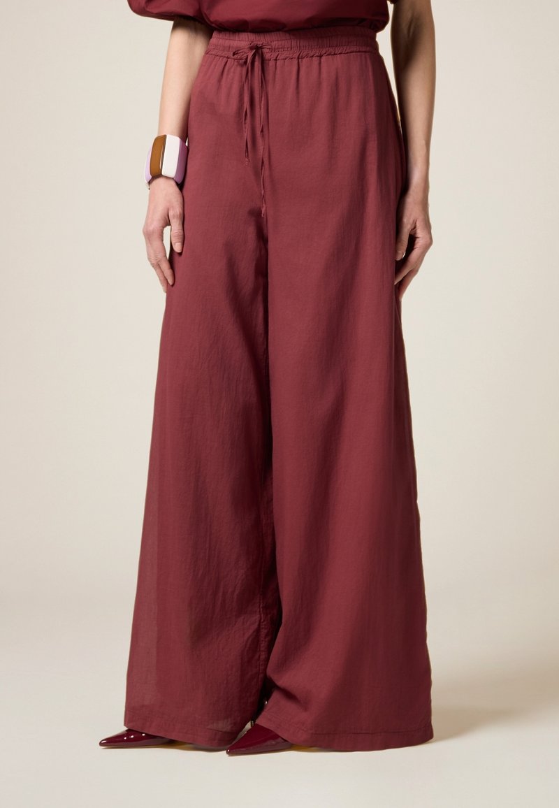 Brede burgundy broek van lichtgewicht stof met een elastische tailleband en koord. Gecombineerd met puntige rode hakken en een multicolor armband.