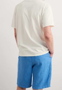 Camiseta corta de color beige claro, con cuello redondo, combinada con pantalones cortos de lino azules que tienen bolsillos laterales y un corte relajado.