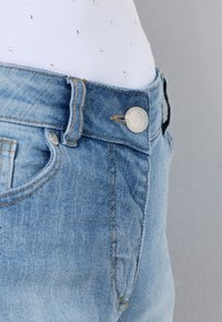 Světle modré džínové kalhoty se zapínáním na kovový knoflík a přední kapsou. Nabízí jemné vyblednutí a kontrastní šití. Hladká textura.