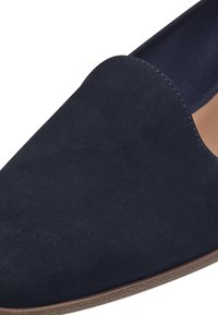 Tengerészkék velúr slip-on cipő hegyes orral és sima textúrával. Minimalista designnal és világosbarna talppal rendelkezik.