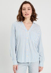 Chemise à rayures bleu clair et crème, avec un col en V, des manches longues, une poche poitrine et une coupe décontractée. Fabriquée en tissu doux.