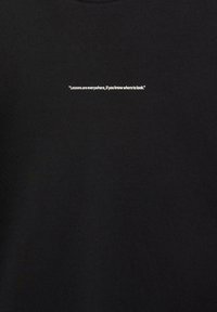 Sort bomulds t-shirt med rund hals og en hvid tekstprint på fronten, der står: "Lektioner er overalt, hvis du ved, hvor du skal kigge."