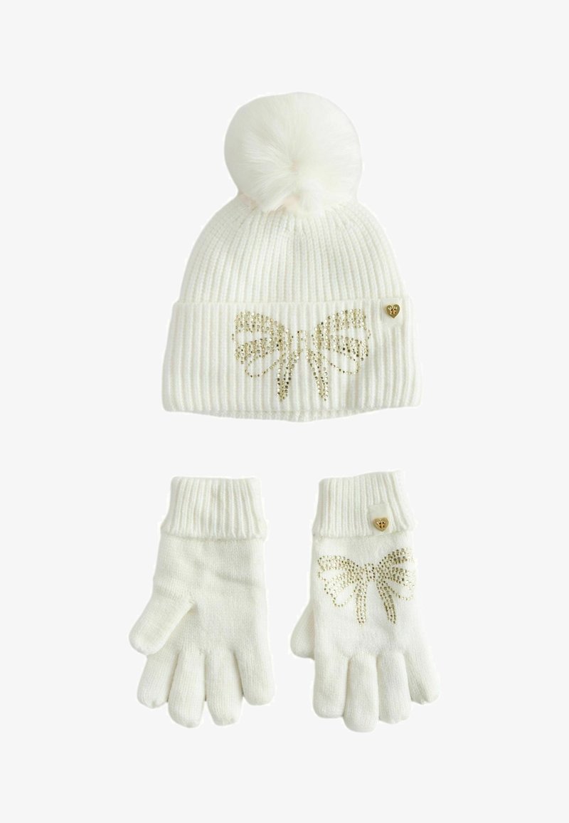 Gorro de punto blanco acanalado con pompón y diseño de mariposa dorada; guantes a juego con un patrón similar y un pequeño acento de corazón dorado.