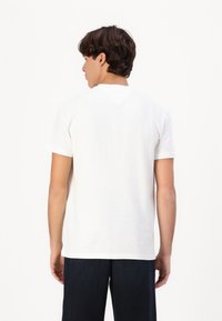 Witte katoenen T-shirt met korte mouwen en een V-vormige achterhalsdetail, gecombineerd met donkere broek, gezien vanaf de achterkant.