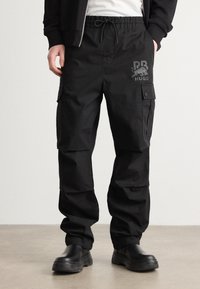 Svarte cargobukser med snor i midjen, med sidelommer, en matt logo på låret og en ledig passform. Laget av slitesterkt stoff.