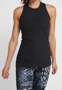 Svart ribbad linne med hög krage och ärmlös design, tillsammans med mönstrade leggings i nyanser av blått och vitt.