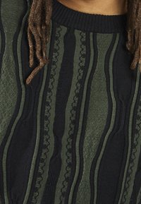 Strickpullover mit abwechselnd dunklen grünen und schwarzen Streifen, der strukturierte Muster und einen gerippten Ausschnitt aufweist. Weicher Stoff, Rundhalsausschnitt-Design.